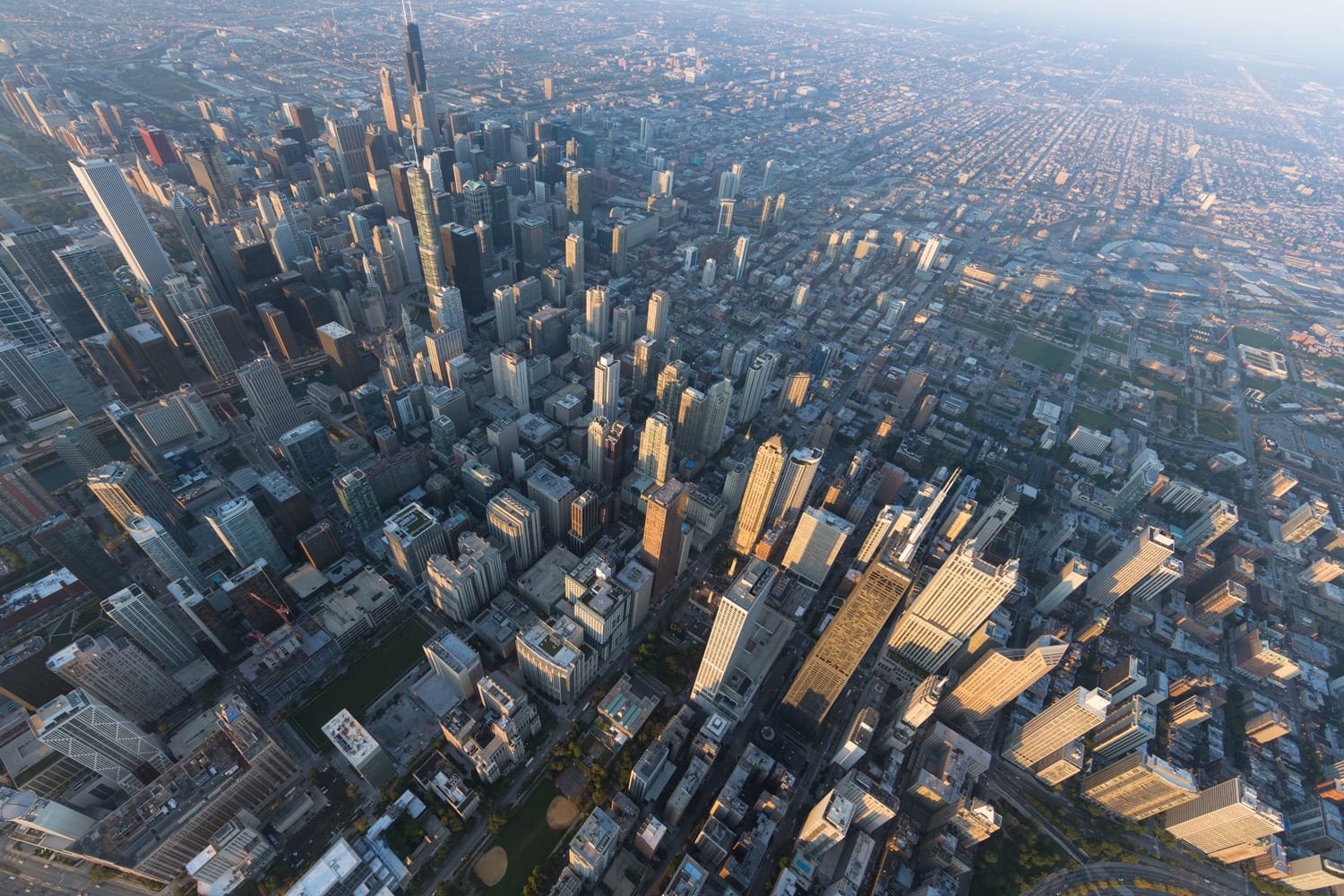 Aerial view of a city skyline with tall skyscrapers and sprawling urban landscape under a clear blue sky.