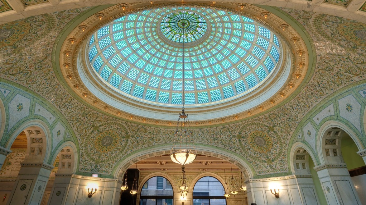 Stunning interior view of a grand hall with a large, intricate stained glass dome ceiling and ornate decorative details.