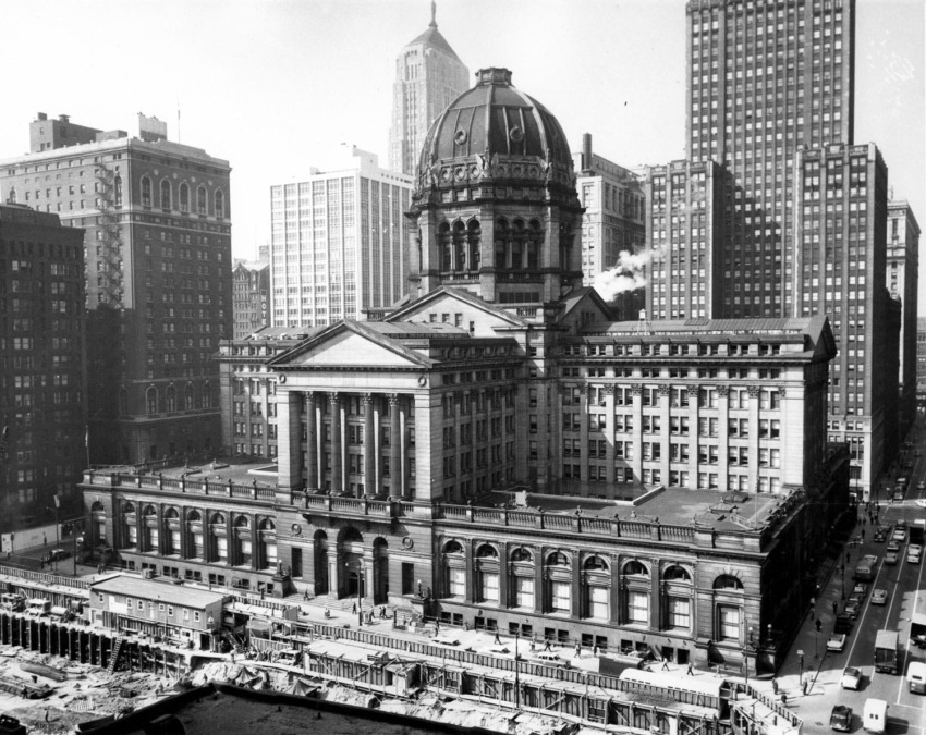 Historic courthouse building surrounded by skyscrapers in a busy cityscape, captured in a black and white photograph.