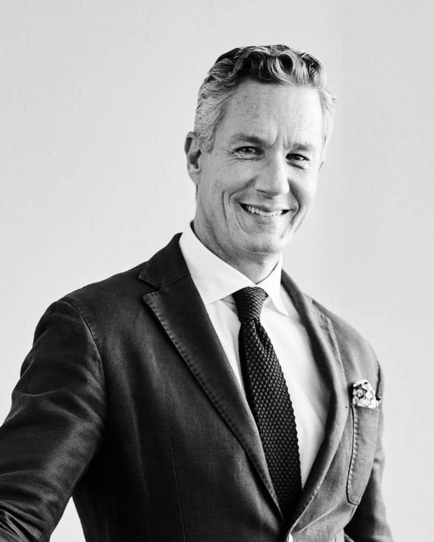 Smiling man in a suit and tie against a plain background, showcasing confidence and style.