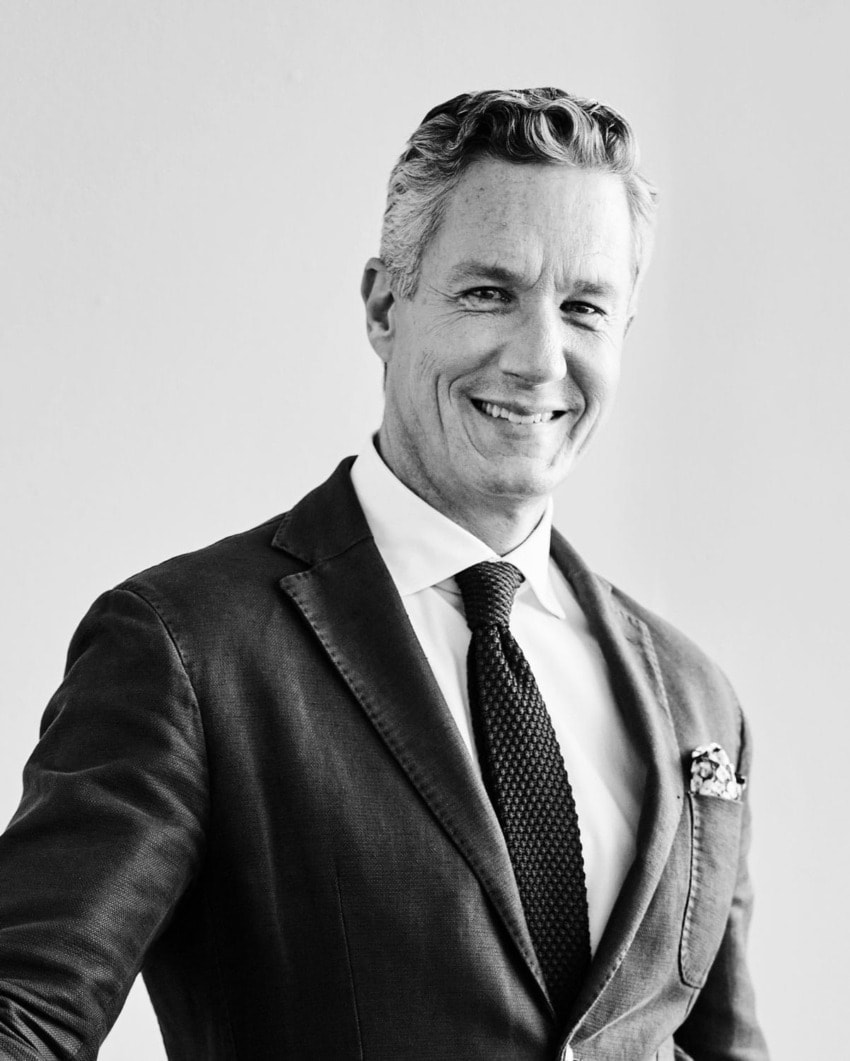 Smiling man in a suit and tie against a plain background, showcasing confidence and style.