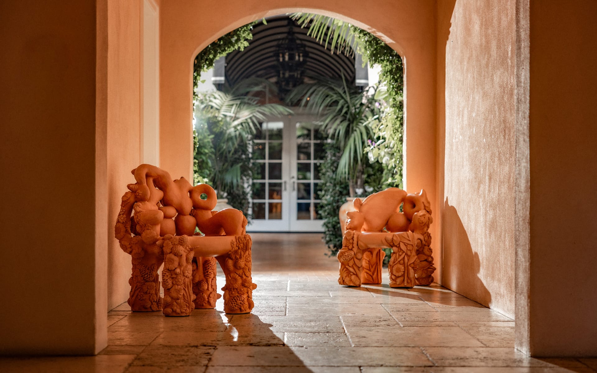 Two artistic chairs with sculpted designs in a bright hallway leading to a garden area.