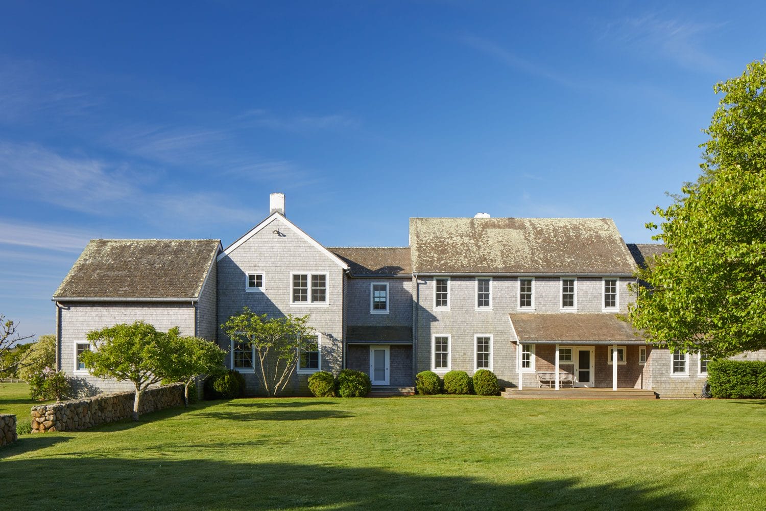 Large country house with a grey exterior and a spacious green lawn under a clear blue sky.