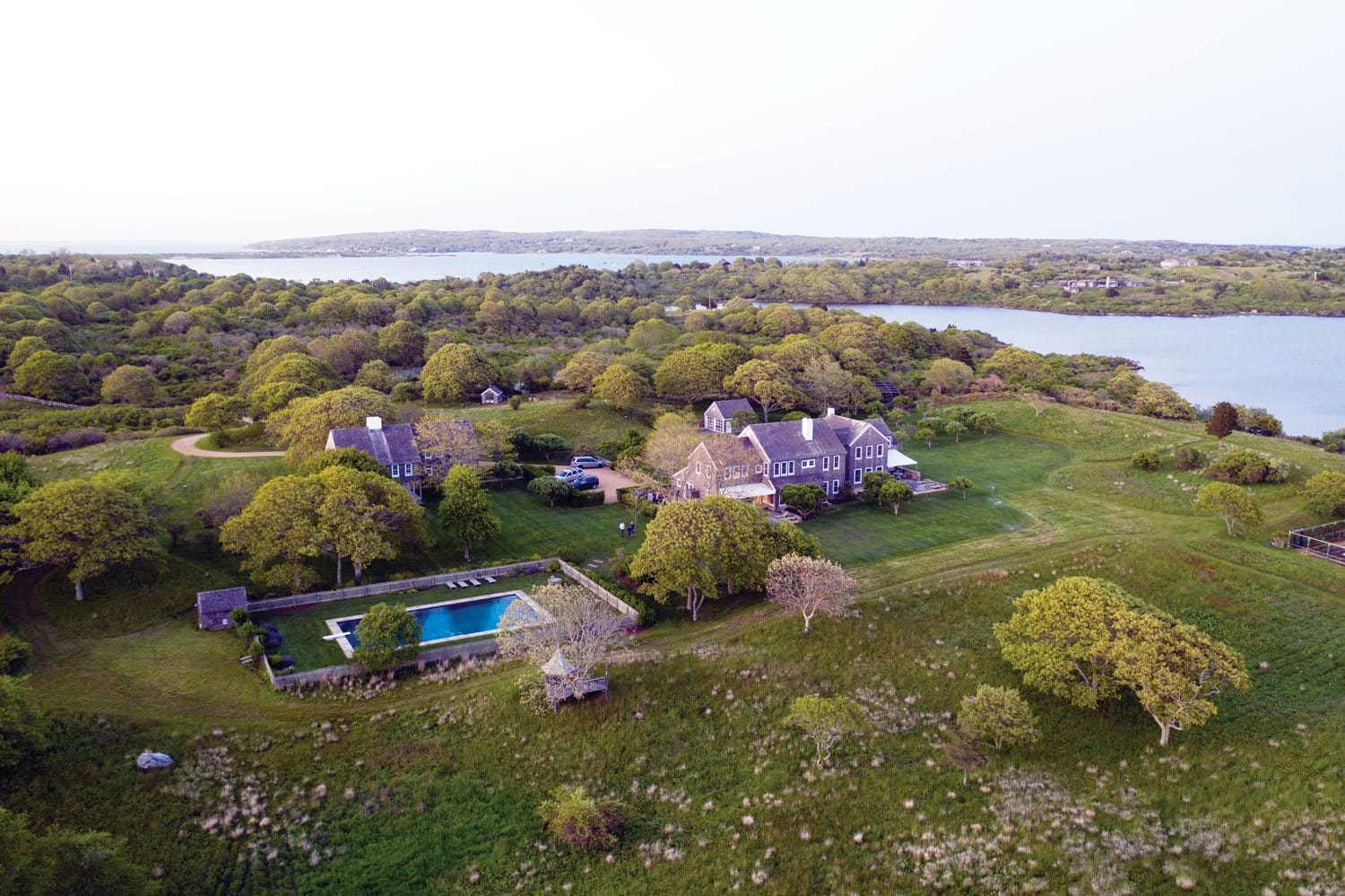 Aerial view of a large estate with a swimming pool, surrounded by lush greenery and a scenic lake in the background.