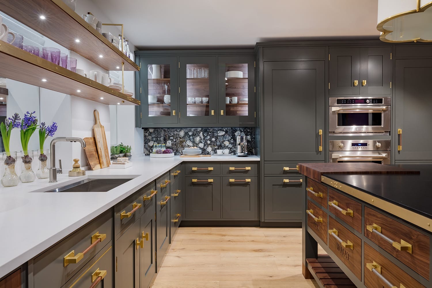 Modern kitchen with dark cabinets, white countertops, and stainless steel appliances, featuring open shelves and floral decor.