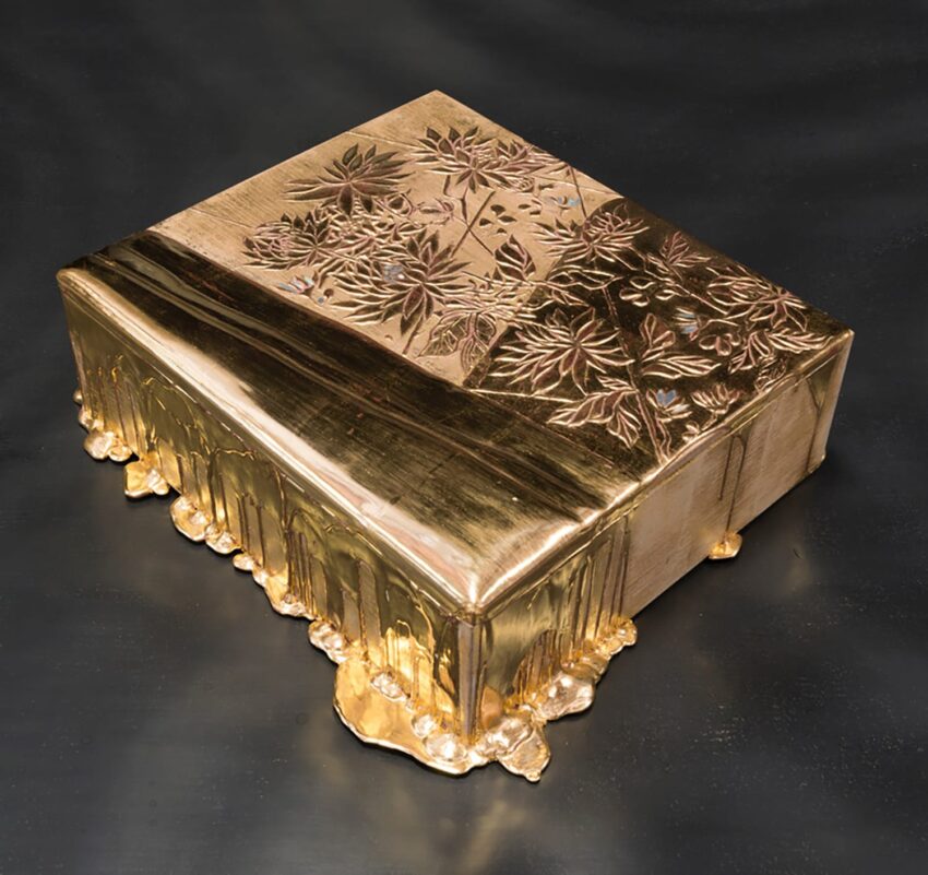 Golden rectangular object with intricate floral engravings and dripping molten texture on a dark background.