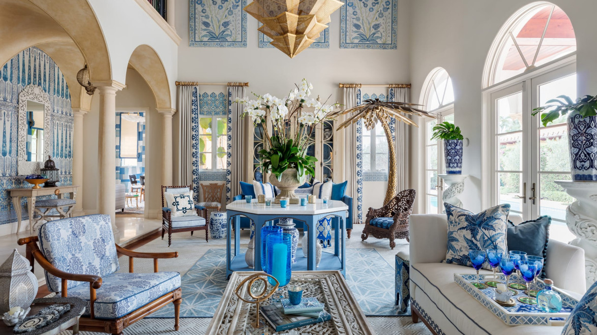 Luxurious living room with blue and white decor, ornate furniture, large windows, and an elegant chandelier.