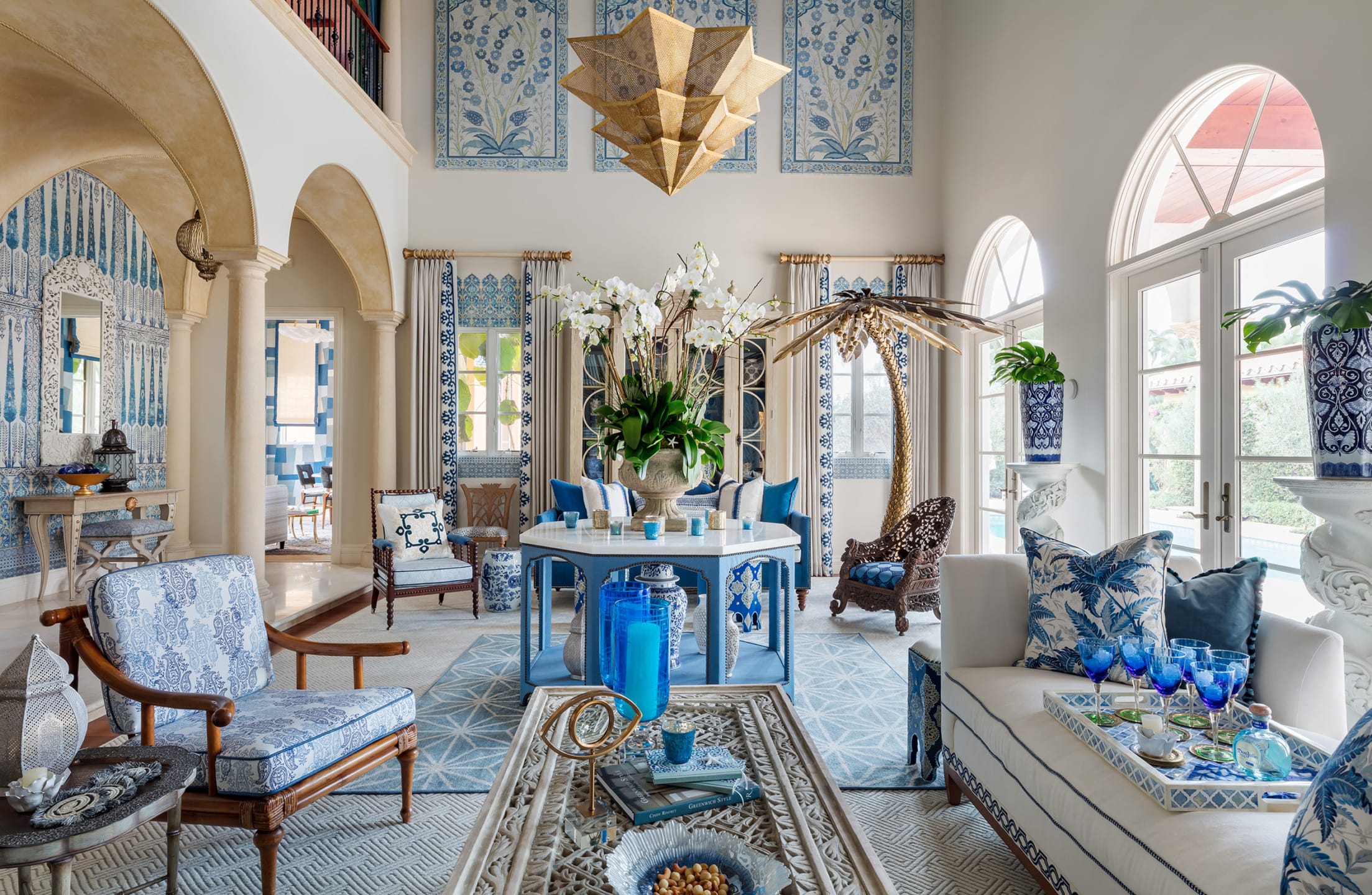 Luxurious living room with blue and white decor, ornate furniture, large windows, and an elegant chandelier.