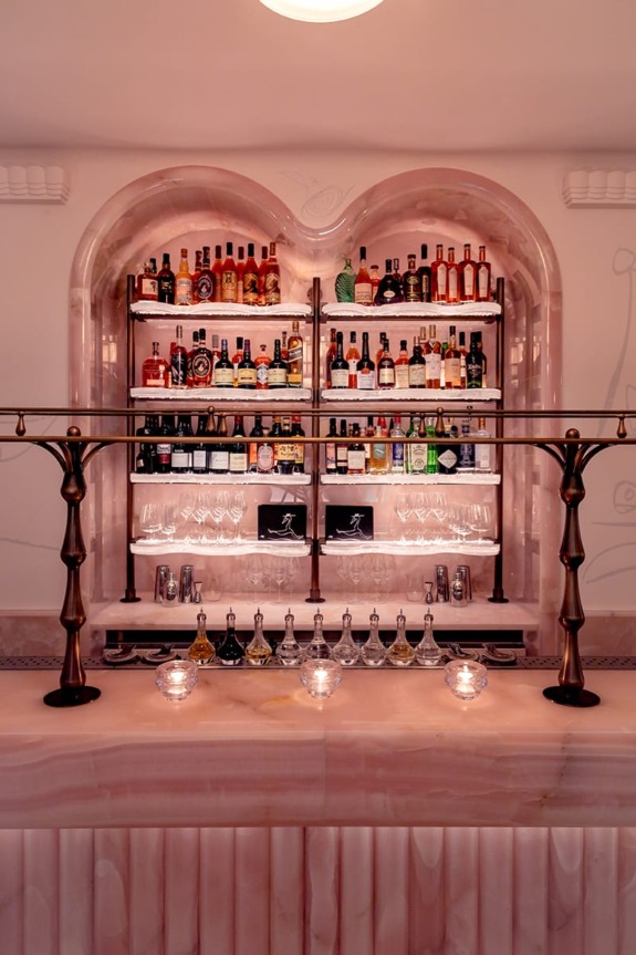 Luxurious pink marble bar with a variety of liquor bottles and glassware displayed on shelves in an elegant setting.
