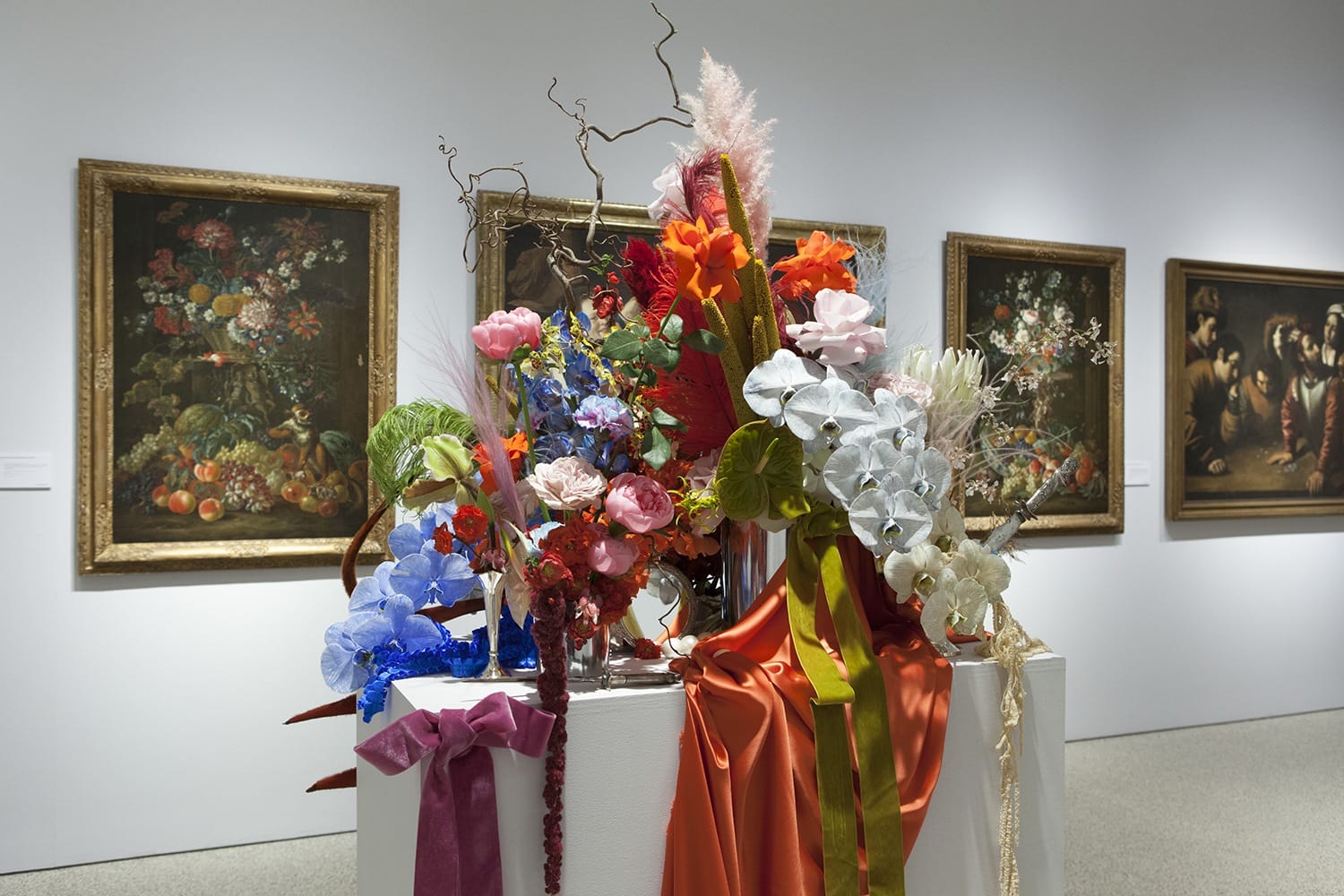 Colorful floral arrangement with ribbons in a gallery, paintings on wall in background