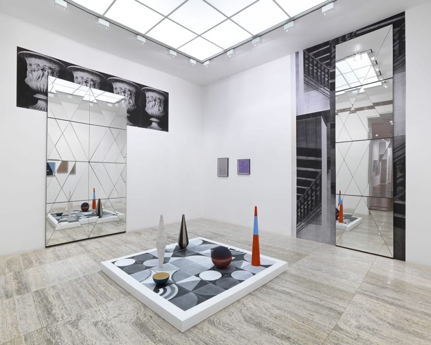 Modern art gallery with geometric sculptures, large mirrors, and minimalist wall art in a spacious, well-lit room.