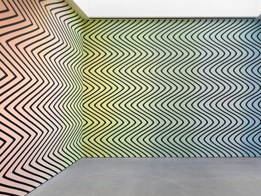 Abstract wall art with black zigzag lines on colorful gradient background from peach to green to blue in a corner setting.