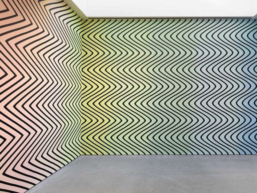 Abstract wall art with black zigzag lines on colorful gradient background from peach to green to blue in a corner setting.