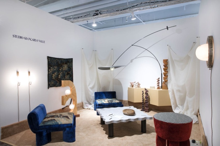 Contemporary art installation with modern furniture, abstract sculptures, and fabric drapes in a gallery space.