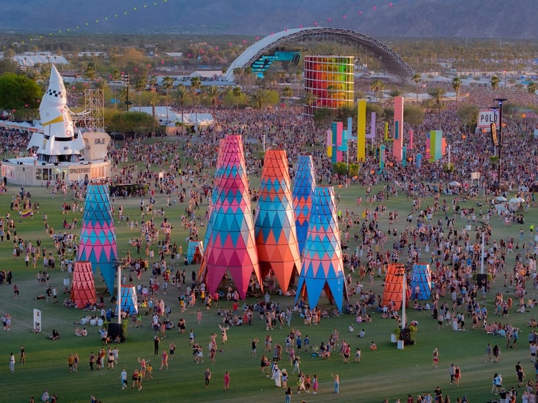 Aerial view of a vibrant outdoor music festival with colorful structures and a large crowd surrounded by mountains.