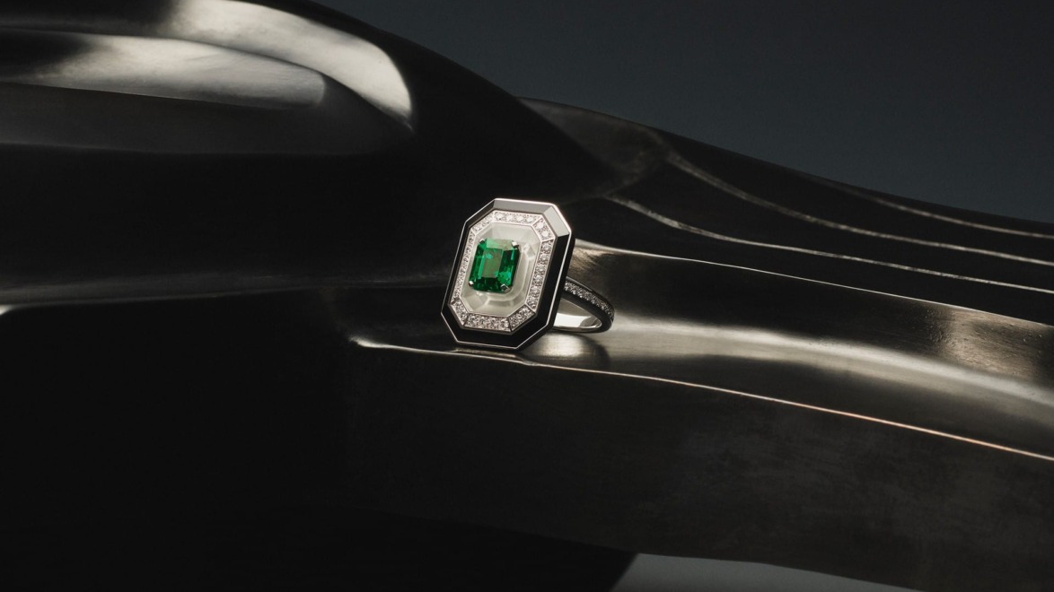 Emerald-cut ring with green gemstone and diamond accents on sleek, curved black surface background.