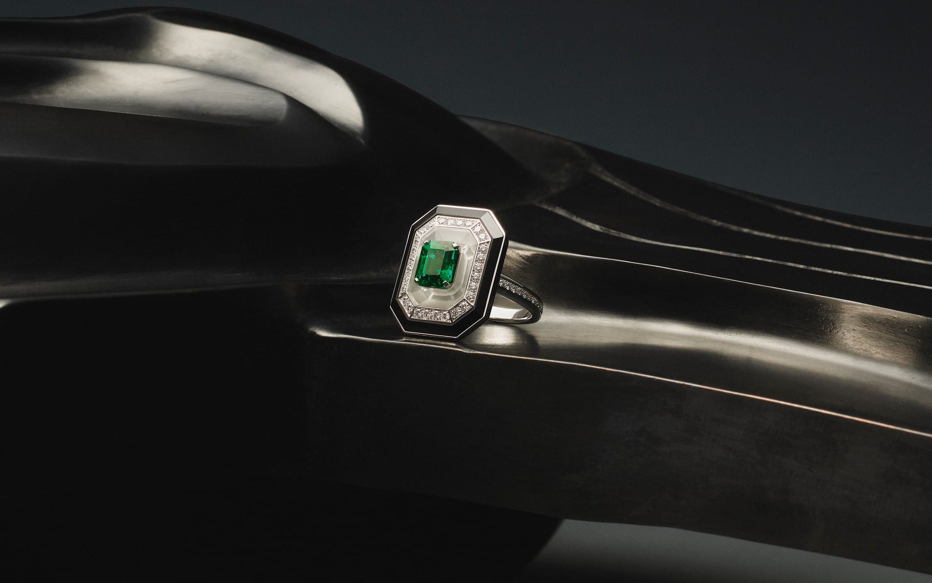 Emerald-cut ring with green gemstone and diamond accents on sleek, curved black surface background.