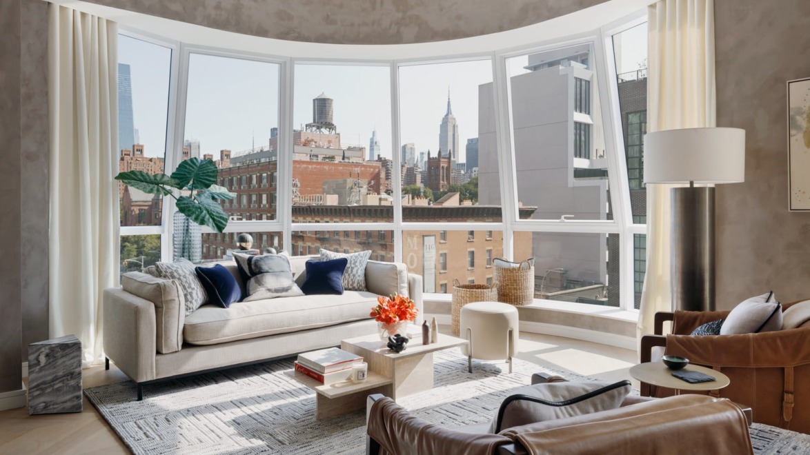 Modern living room with large windows, cityscape views, and stylish furniture including a beige sofa and leather armchairs.