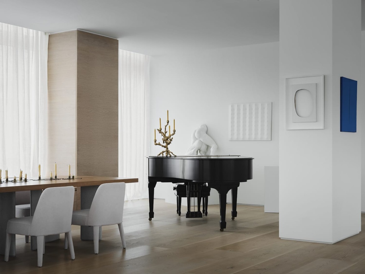 Modern minimalist interior with black grand piano, white chairs, and abstract wall art in a bright room with wood floors.