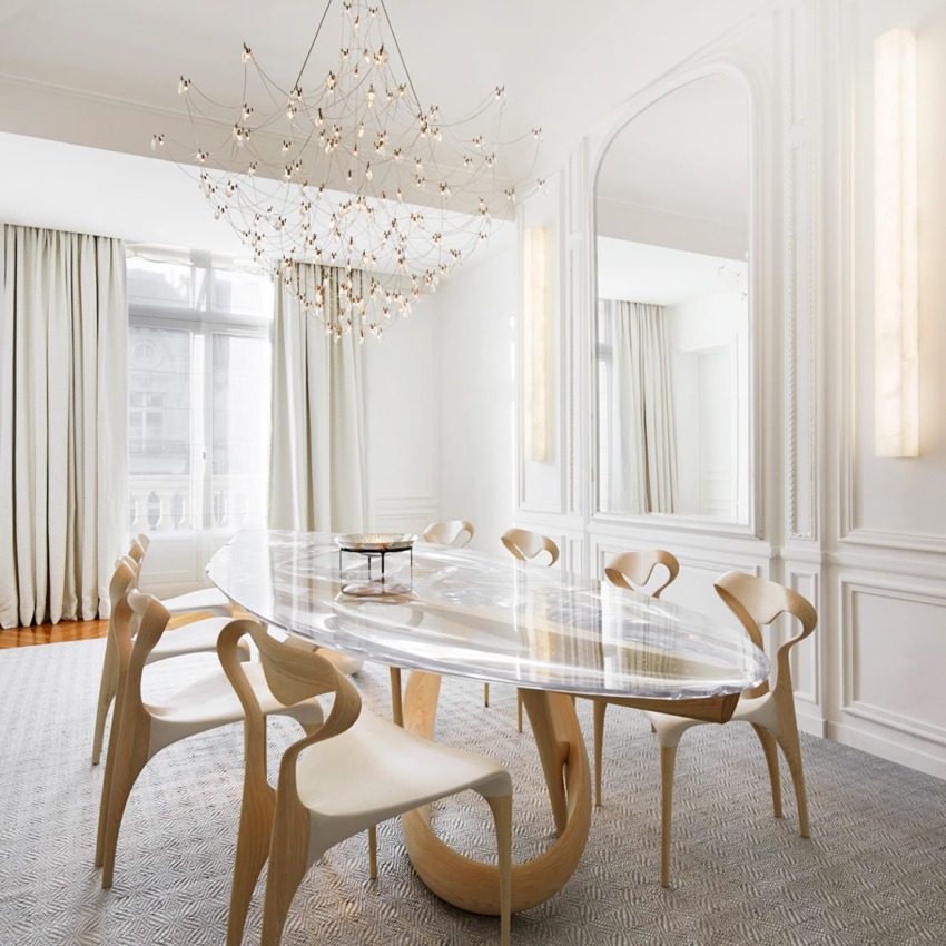 Elegant dining room with oval glass table, modern wooden chairs, large mirror, and intricate chandelier.