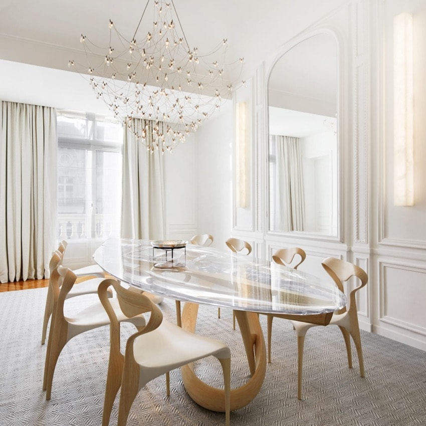 Elegant dining room with oval glass table, modern wooden chairs, large mirror, and intricate chandelier.