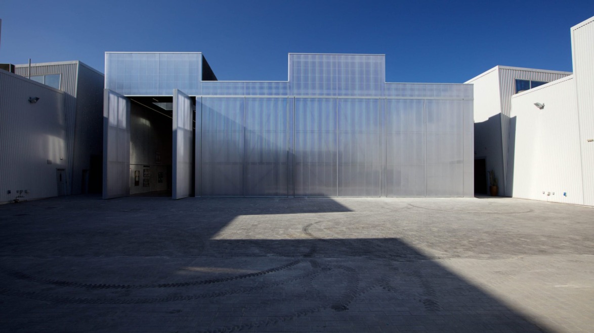 Modern industrial building with large reflective facade under a clear blue sky. Minimalist architectural style.