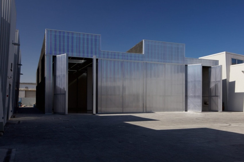 Modern industrial building with large translucent facade, open doors, and clear blue sky background.