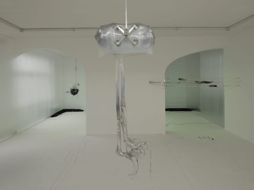 Modern art installation in a minimalist white gallery with hanging metallic sculpture and abstract elements on the walls.