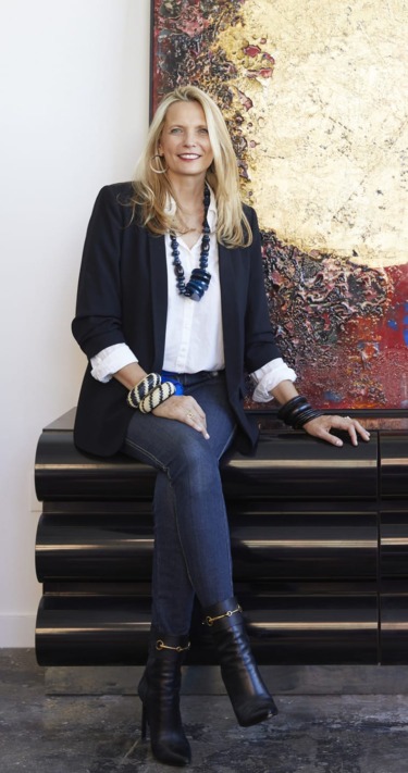 Person sitting on a black bench, wearing jeans and a black blazer, with a large abstract painting in the background.