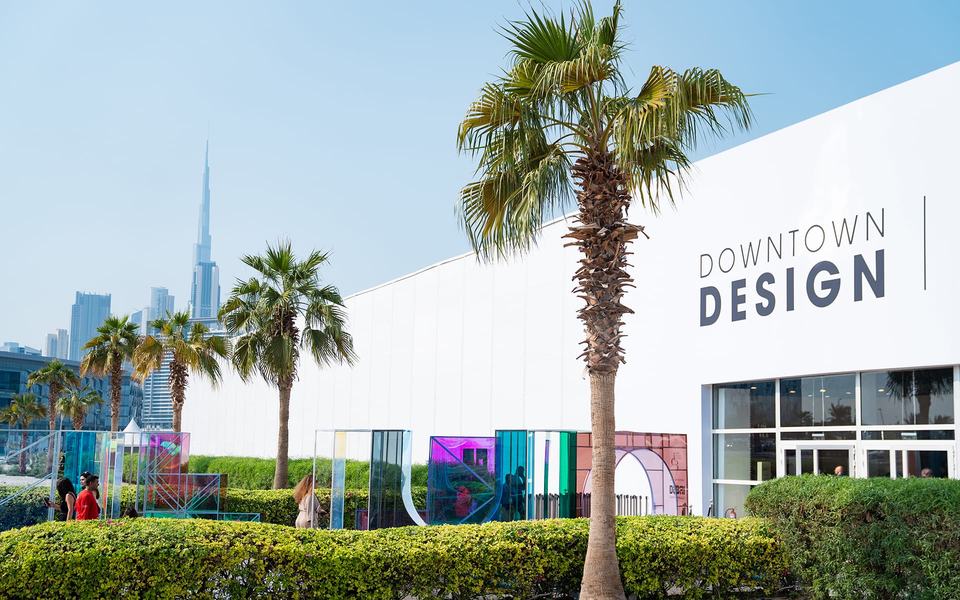 Modern building with 'Downtown Design' signage, palm trees, and colorful structures, set against a cityscape background.