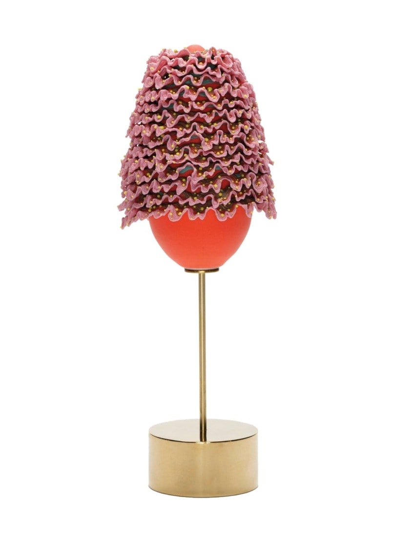 Egg-shaped sculpture with pink ruffled layers on top, mounted on a brass stand with a round base.