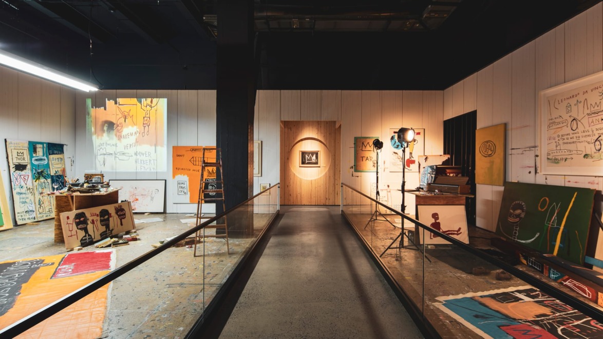Art gallery with various colorful paintings and drawings displayed on walls and floor, featuring eclectic modern artworks.