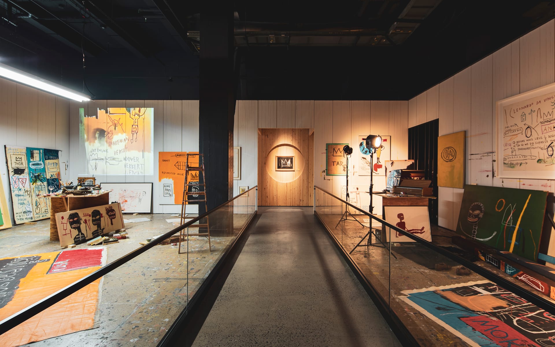 Art gallery with various colorful paintings and drawings displayed on walls and floor, featuring eclectic modern artworks.