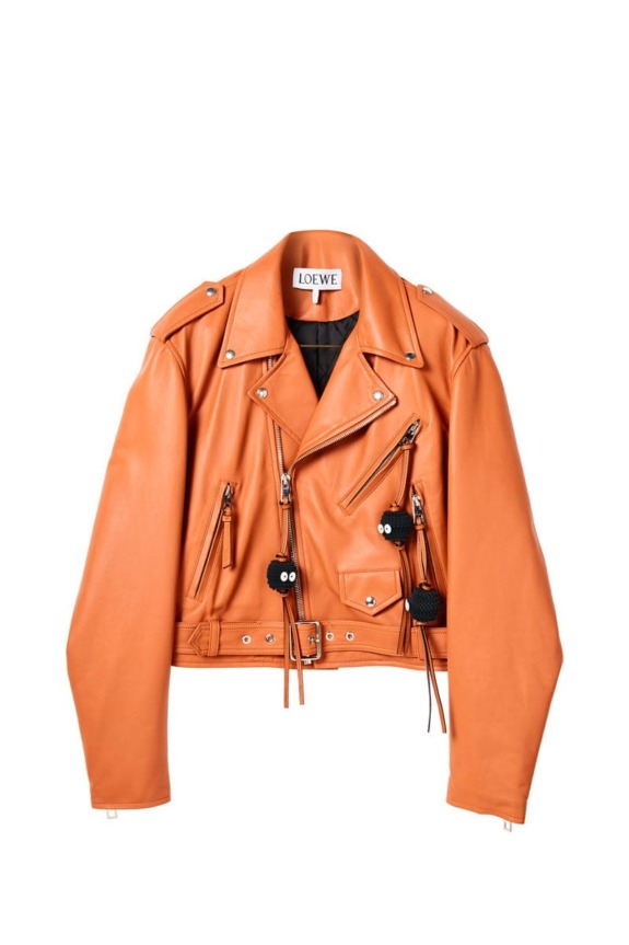 Orange leather biker jacket with multiple zippers and unique black pom-pom accents, displayed on a white background.