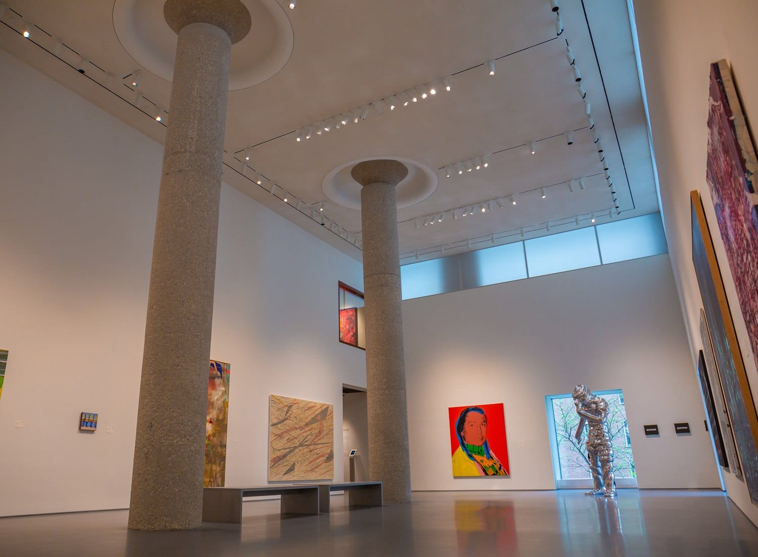 Art gallery interior with tall columns, colorful paintings on walls, and a shiny silver sculpture.