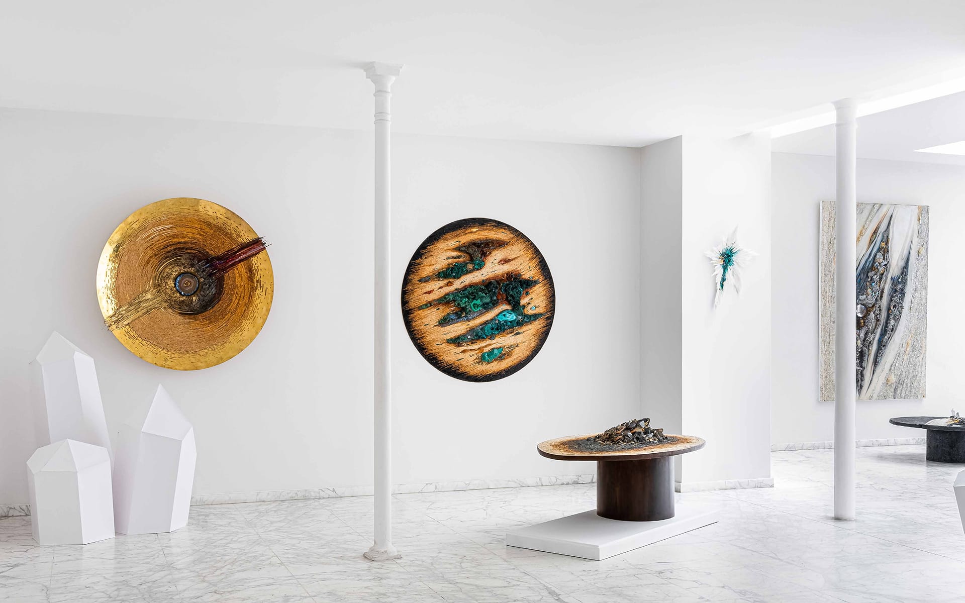 Modern art gallery interior with circular wall art, abstract sculptures, and a marble floor.