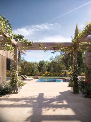 Sunny outdoor pool area with wooden pergola, flowers, trees, and lounge chairs in a serene garden setting.