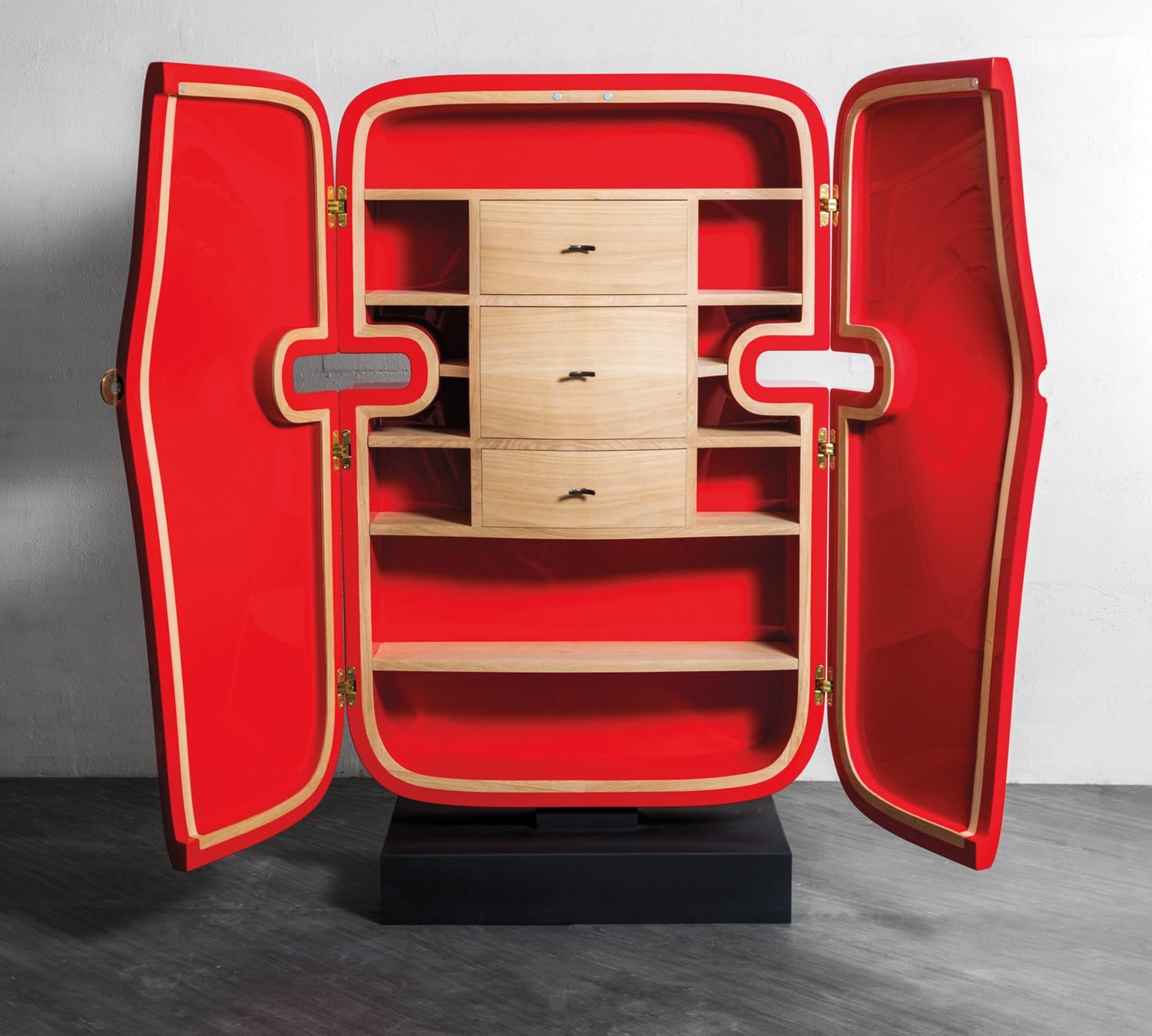 Contemporary cabinet with bright red interior, open to reveal shelves and three central drawers, set against a neutral background.