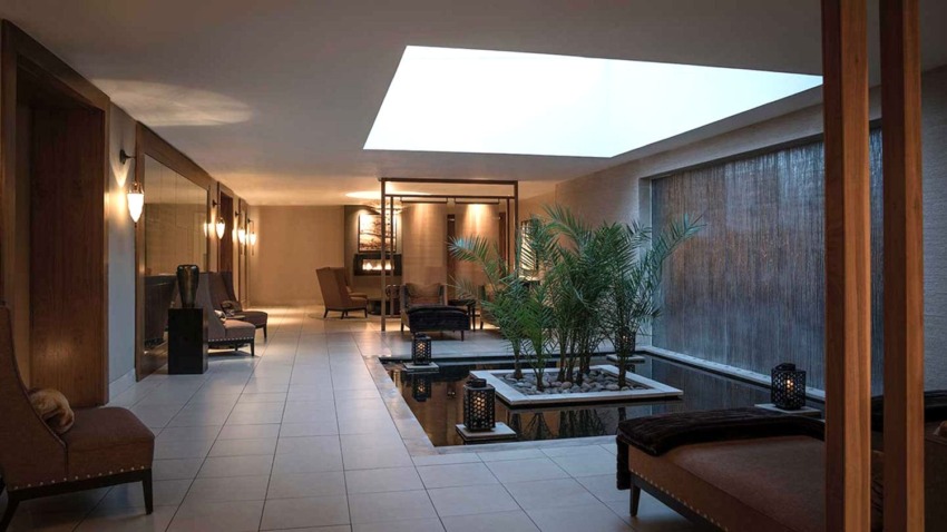 Luxurious spa interior with modern design, featuring lounge chairs, water feature, and indoor palm plants.