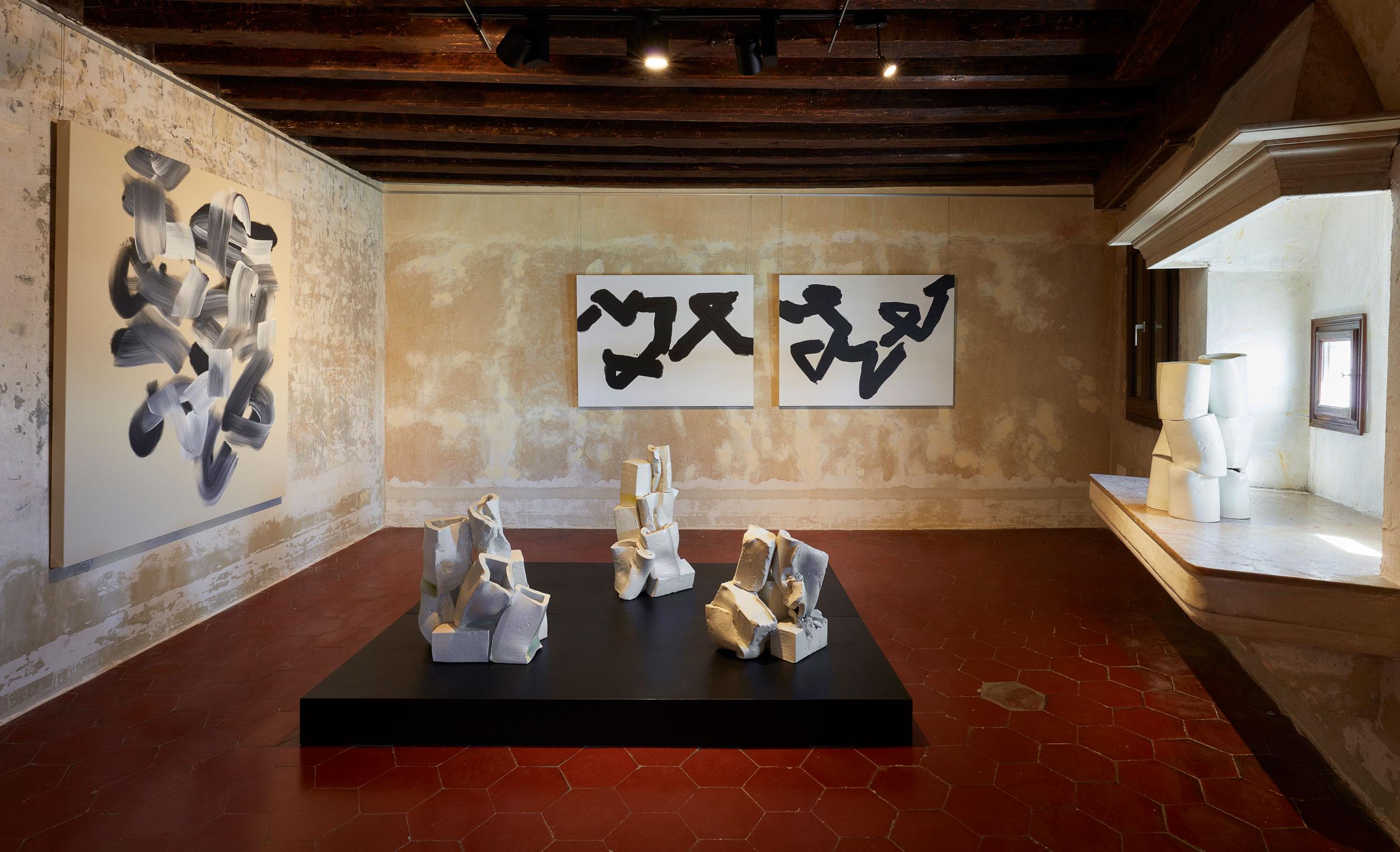 Contemporary art gallery with abstract black and white paintings and sculptural pieces on display in a rustic room.