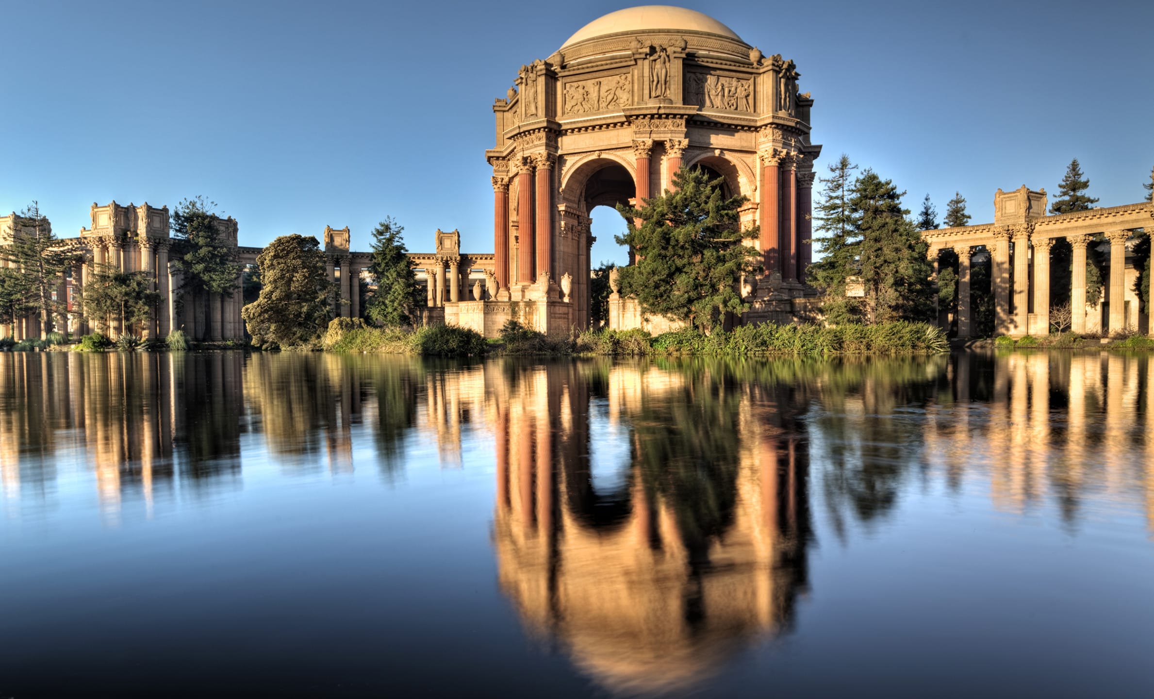 Scenic view of the Palace of Fine Arts in San Francisco with blue sky and reflection in the calm water of the lagoon.