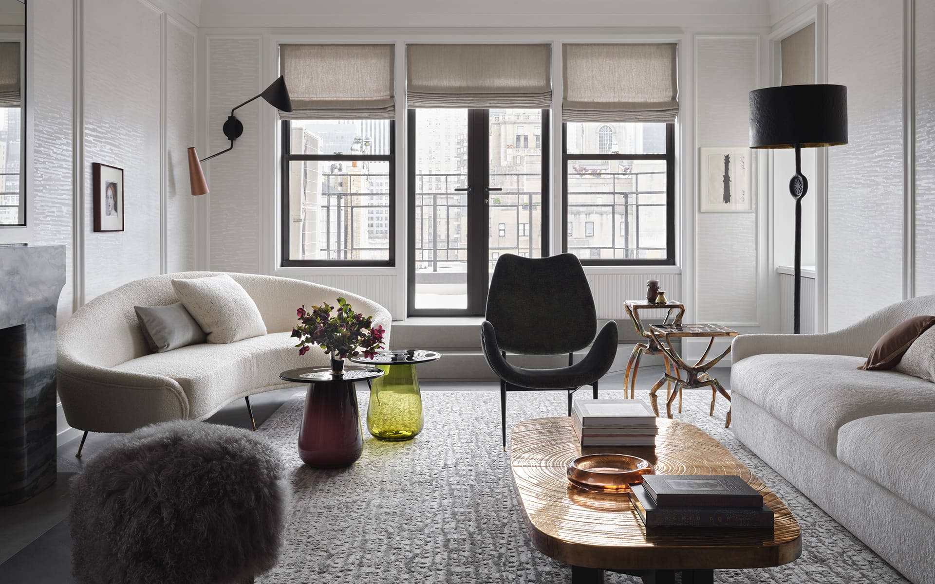 Modern living room with stylish furniture, large windows, neutral tones, and decorative elements like flowers and books.