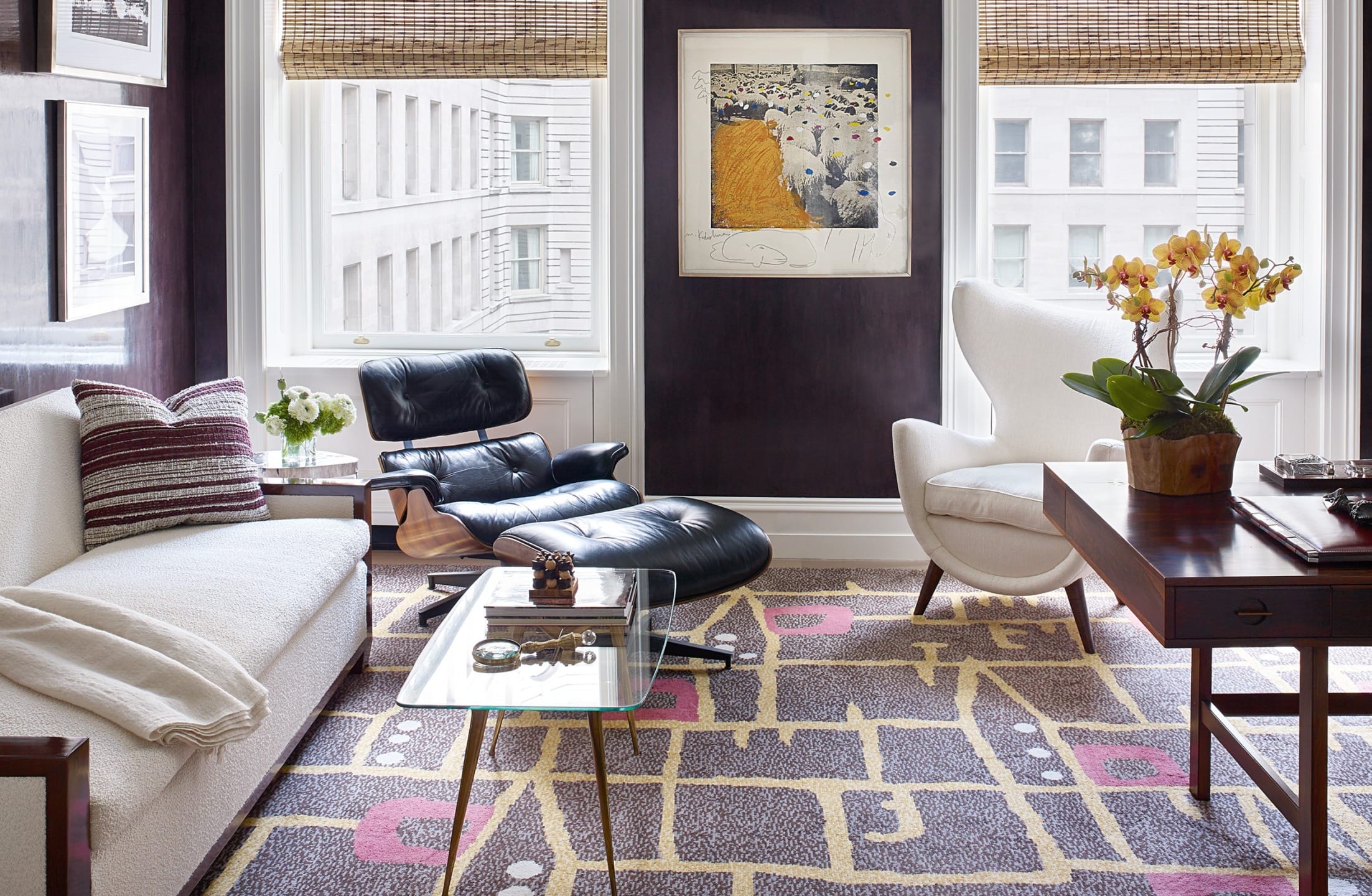 Modern living room with white sofa, black lounge chair, abstract rug, and large windows overlooking city buildings.