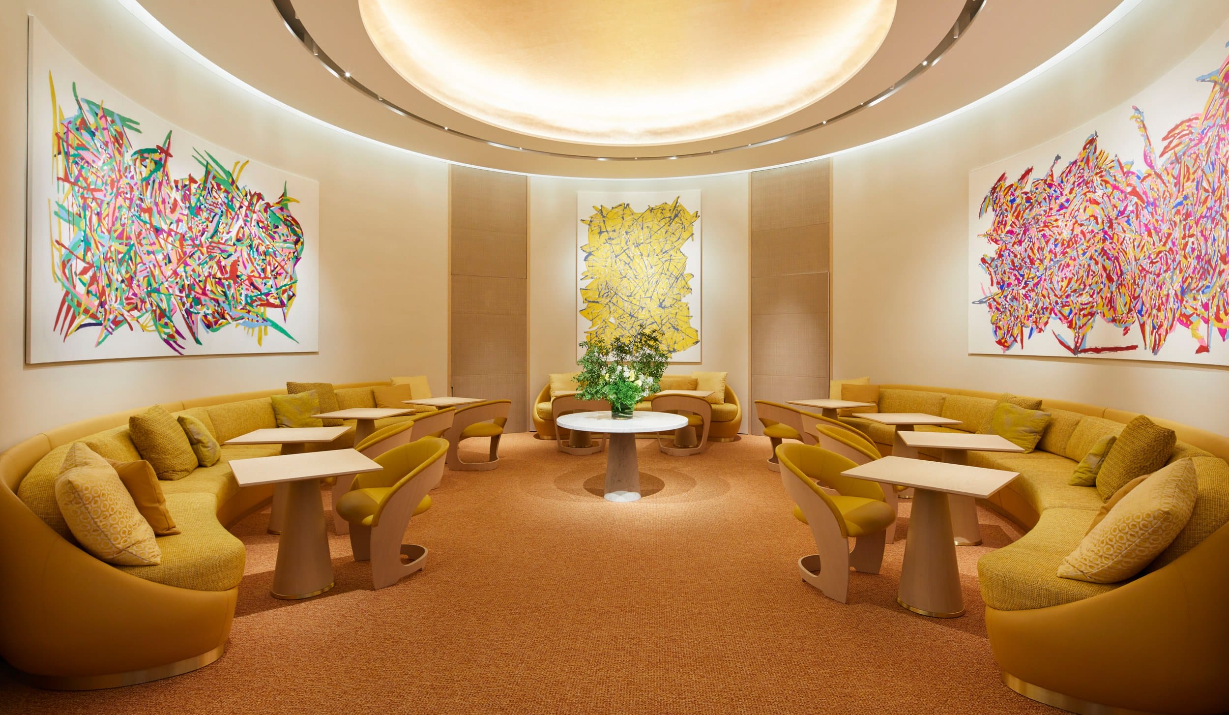 Modern lounge with curved seating, abstract art on walls, a central table with flowers, and soft ambient lighting.