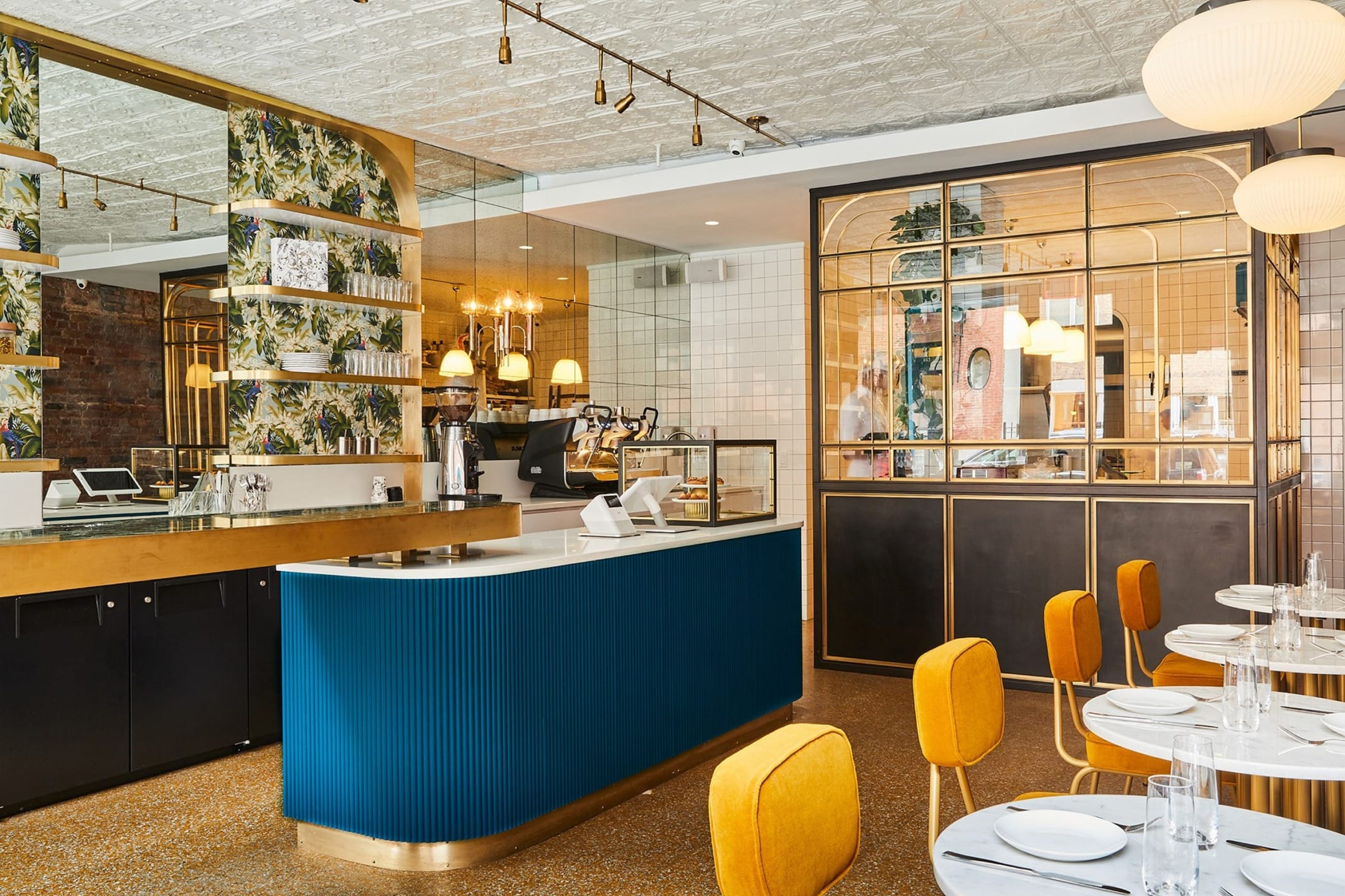 Modern cafe interior with blue counter, yellow chairs, and decorative wallpaper featuring plants.
