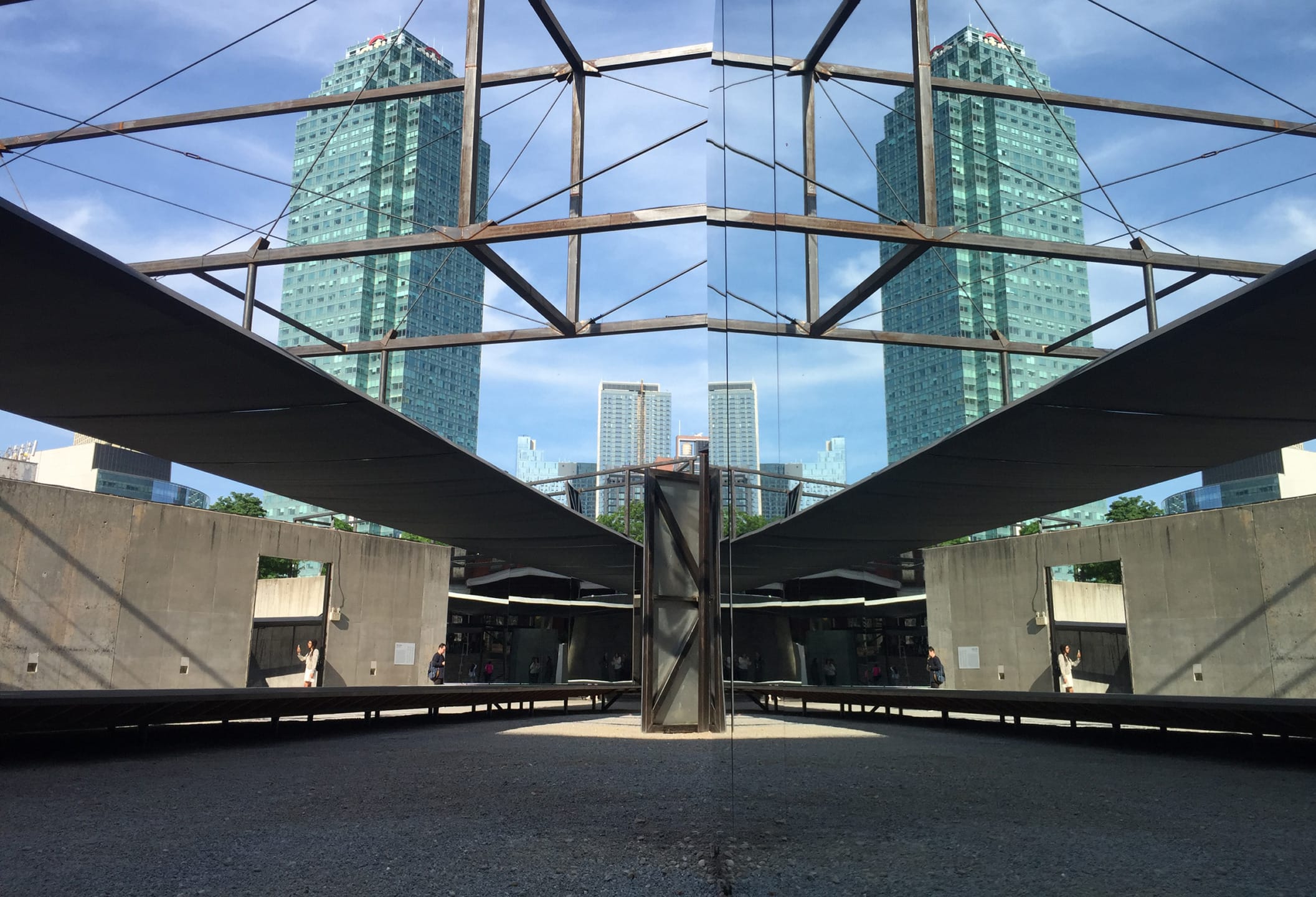 Modern architectural structure with reflective glass surface and tall buildings in the background under a clear blue sky.