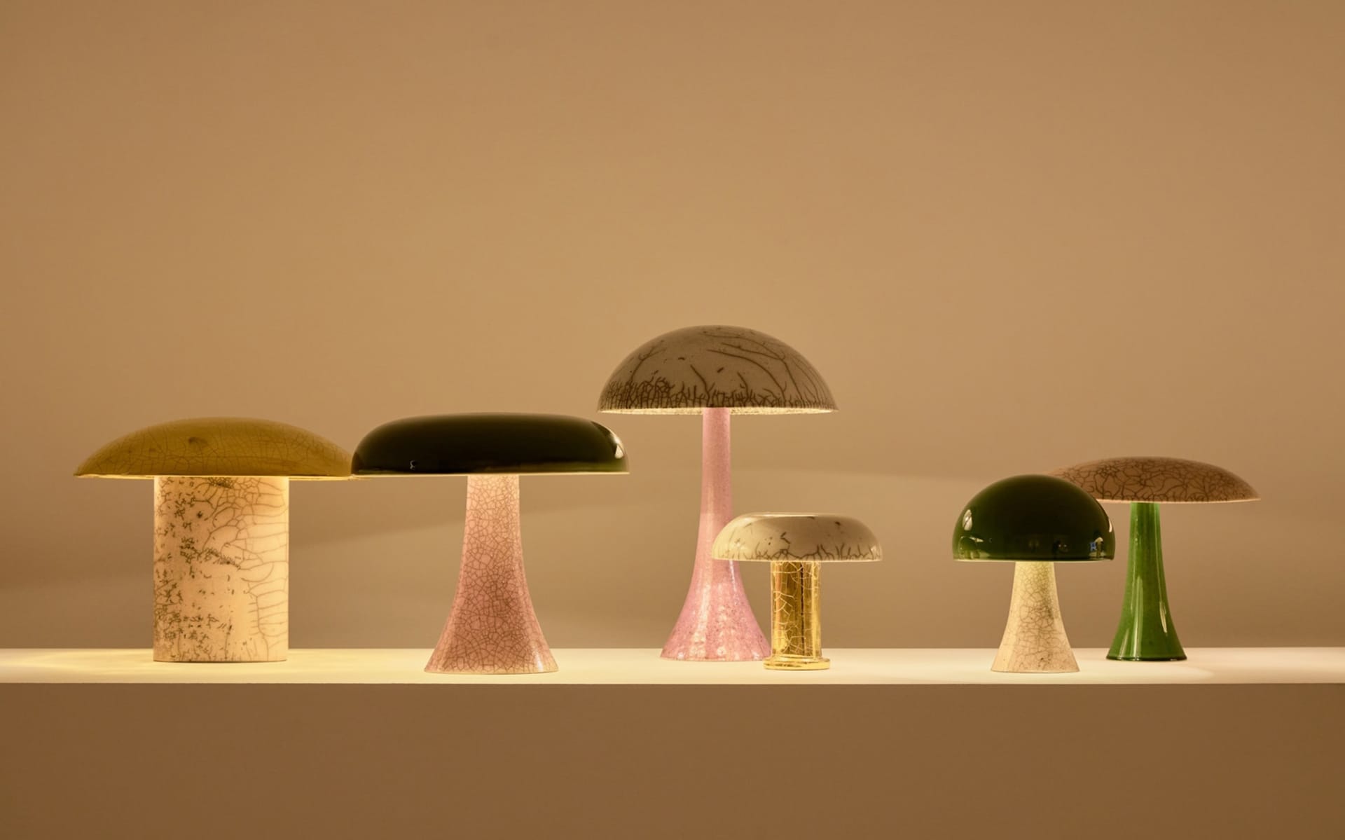 Six colorful mushroom-shaped lamps in varying sizes on a white surface against a warm, neutral background.