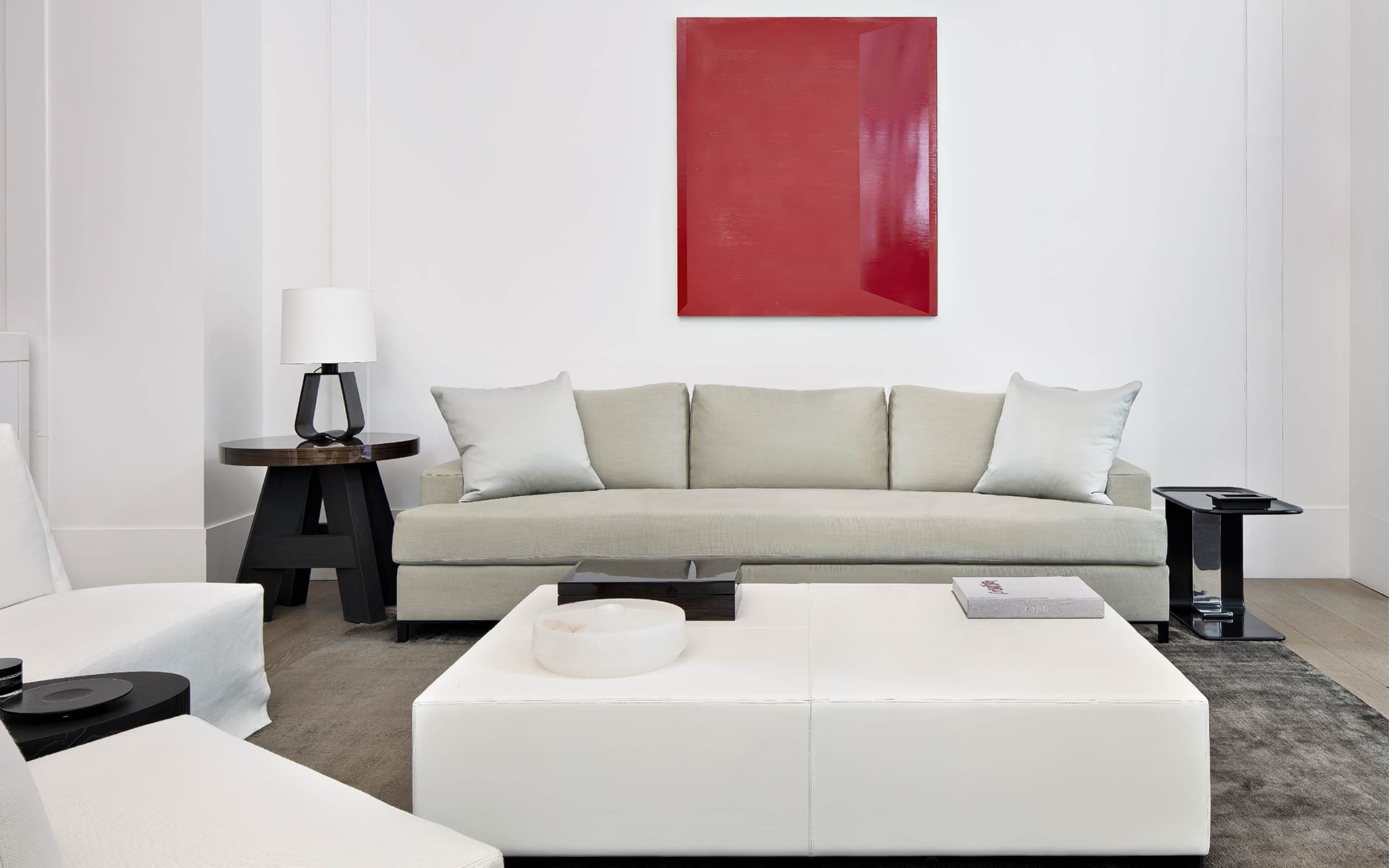 Modern living room with beige sofa, red wall art, white coffee table, and contemporary black side table and lamp.