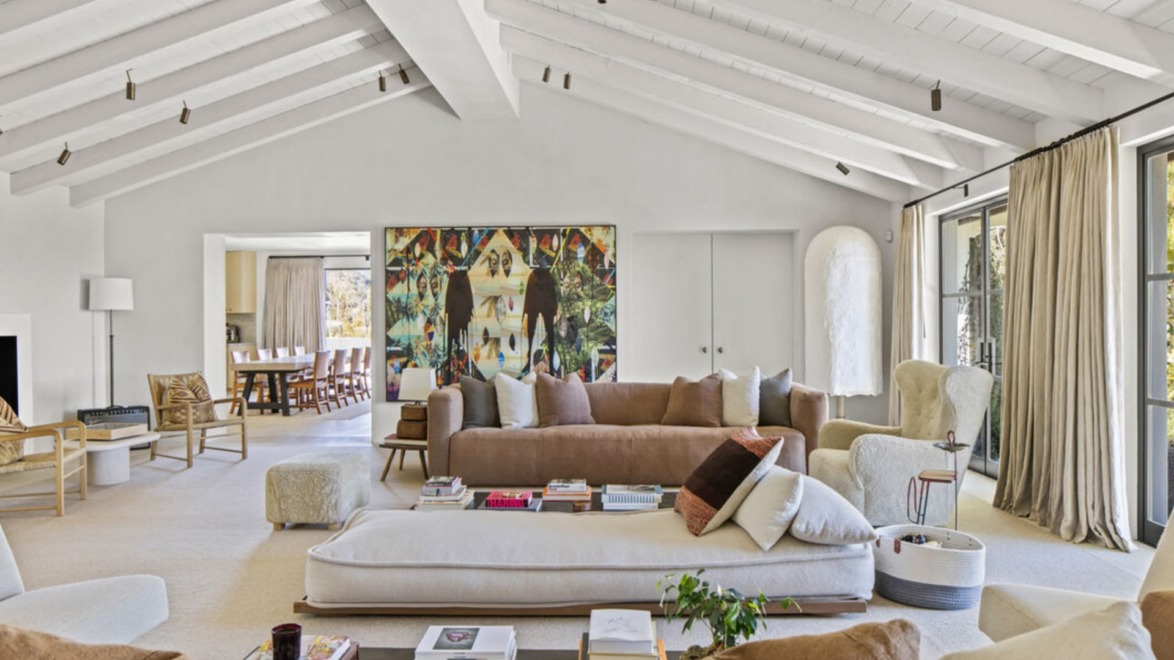 Spacious living room with wooden beams, neutral tones, modern furniture, large artwork, and a view of the dining area.