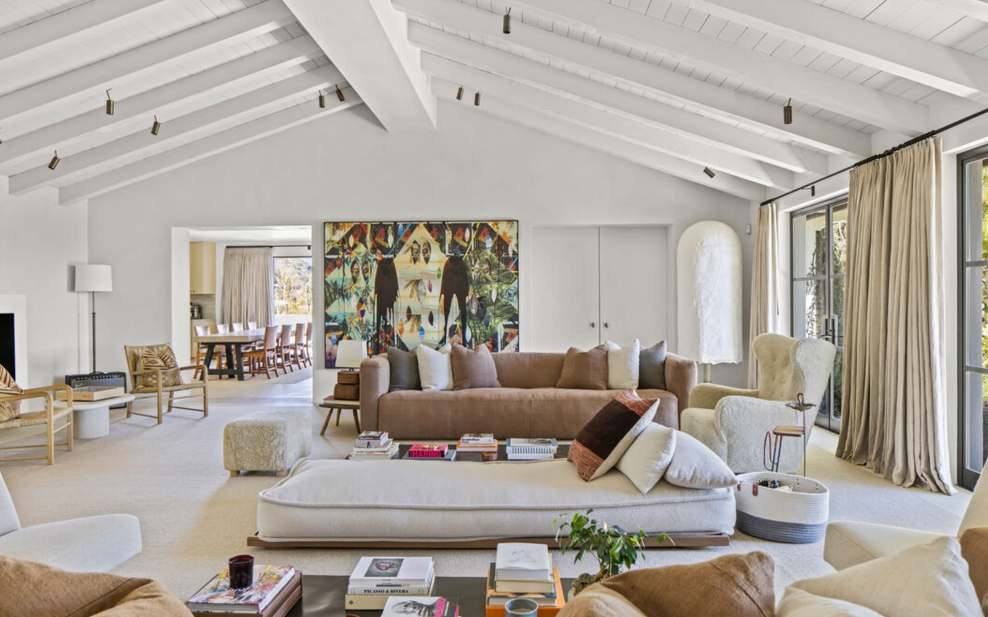 Spacious living room with wooden beams, neutral tones, modern furniture, large artwork, and a view of the dining area.